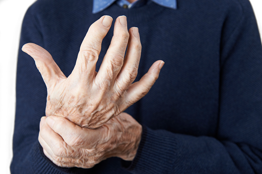 CAR T-cell therapy and RA, senior man in a navy sweater gripping the wrist of his stiff, bent fingers