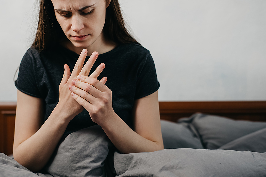 DMARDs vs biologics for rheumatoid arthritis, woman sitting on bed massaging her painful hand and wrist